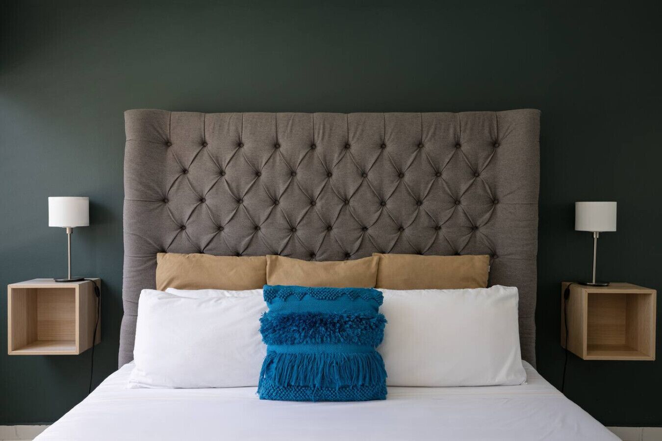 Una cama con cabecera capitonada, dos mesitas de noche y un cojín azul.