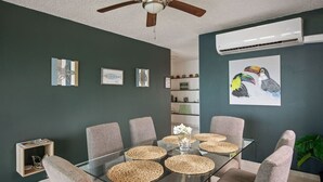 Een eethoek met een glazen tafel, geweven placematen en grijs gestoffeerde stoelen.