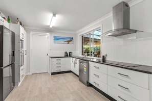 A modern kitchen with white cabinets, a stainless steel range hood, and a window with a view of the outdoors.