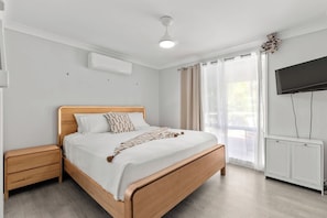 A bedroom with a wooden bed, a nightstand, a TV mounted on the wall, and a window with curtains.