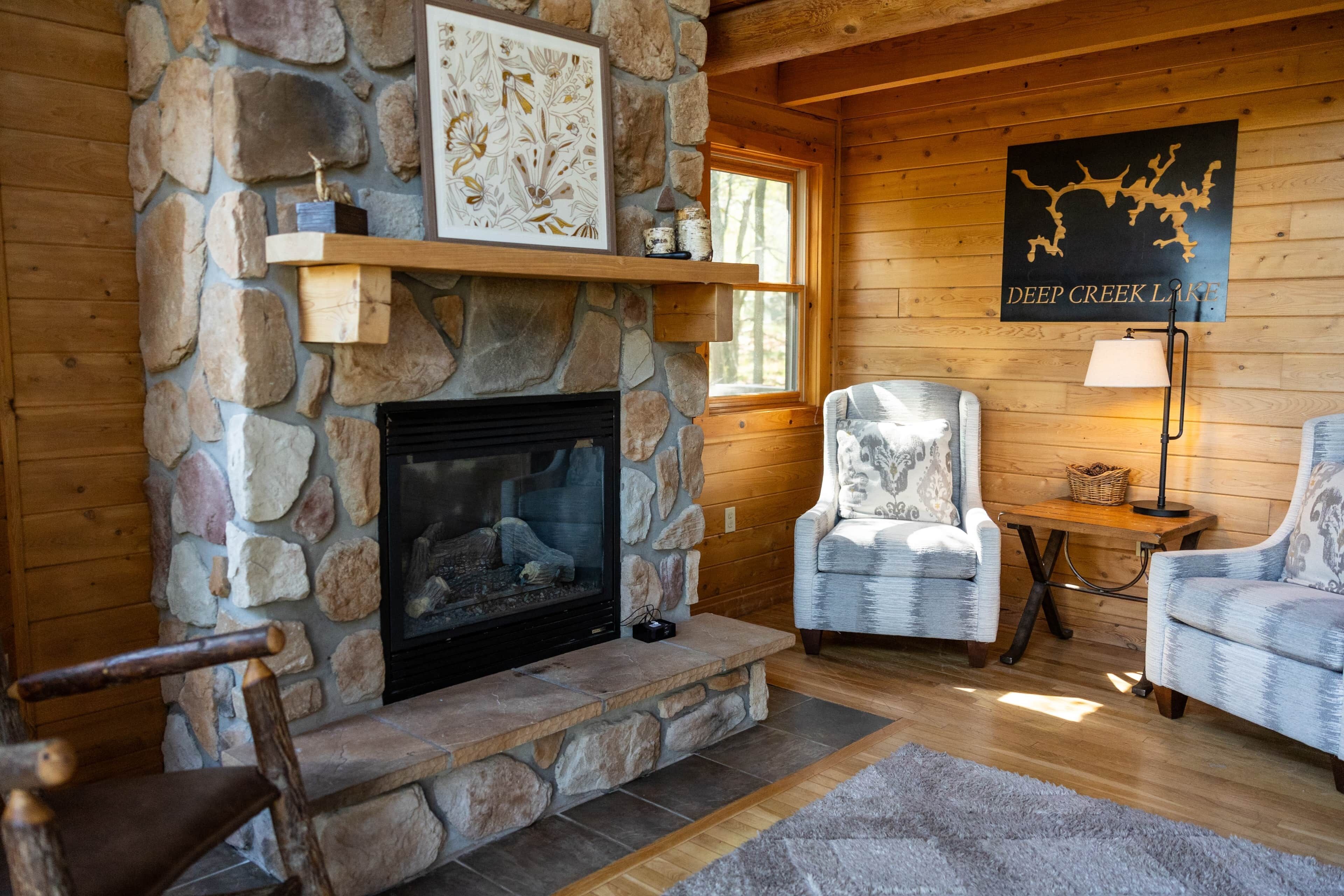 A stone fireplace with a mantel shelf, two upholstered chairs, and a wooden floor.