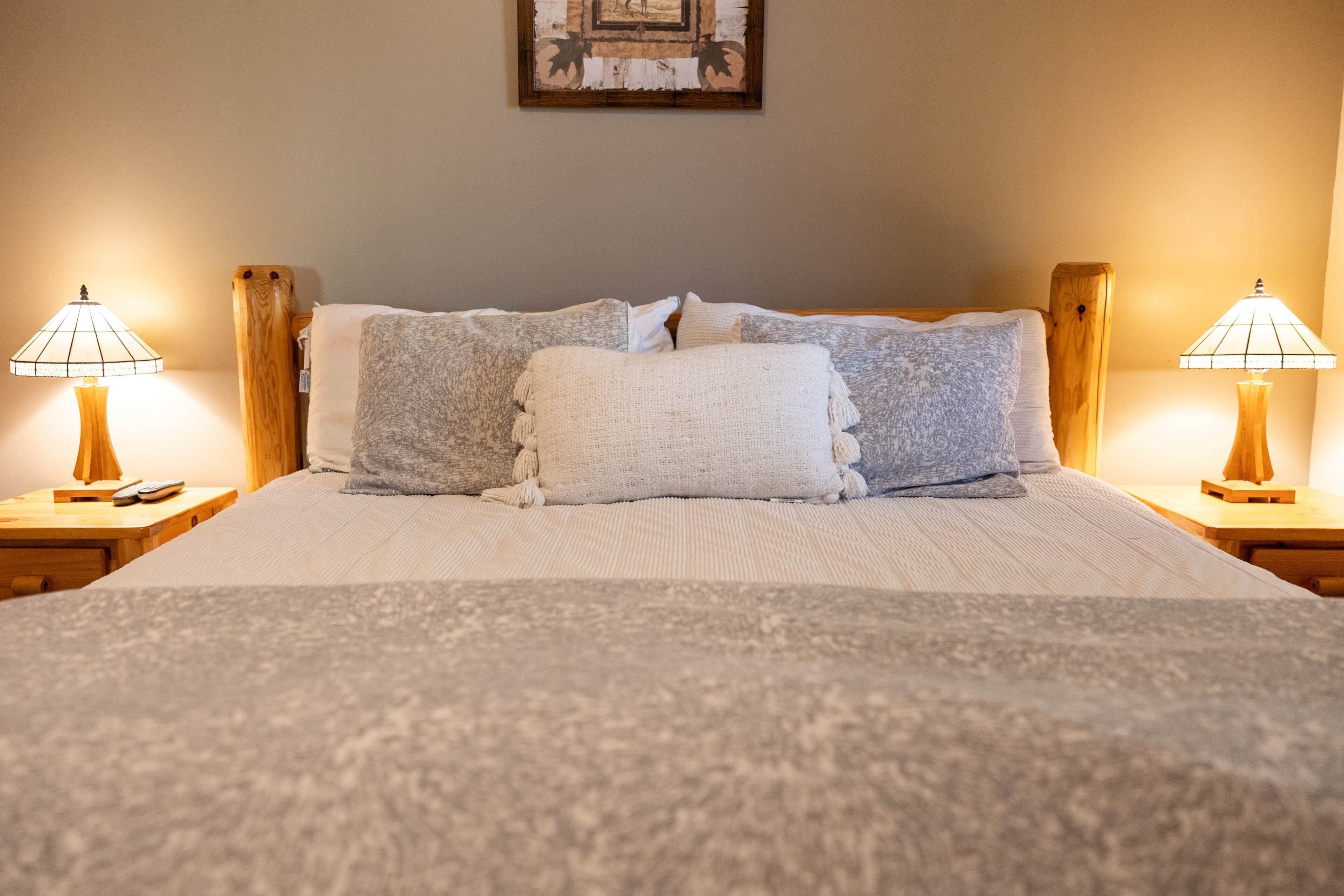 A neatly made bed with a white and gray duvet, two wooden nightstands with lamps, and a framed picture on the wall.