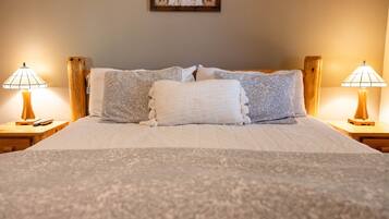 A neatly made bed with a white and gray duvet, two wooden nightstands with lamps, and a framed picture on the wall.