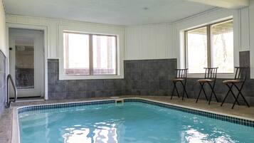 Una piscina interior con paredes de azulejos, una puerta que da al exterior y tres sillas junto a las ventanas.