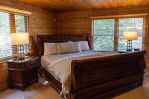Een slaapkamer met houten lambrisering, een groot bed, twee nachtkastjes met lampen en ramen met zonwering.