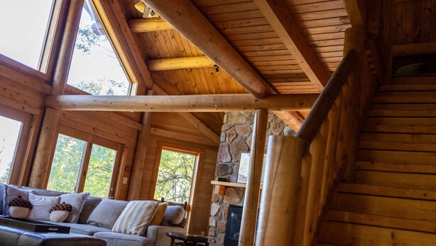 A log cabin interior with a stone fireplace, wooden beams, and a sofa with cushions. - Splash Mountain 6 bedrooms with indoor pool & mountain and filtered lake view (Garrett County)