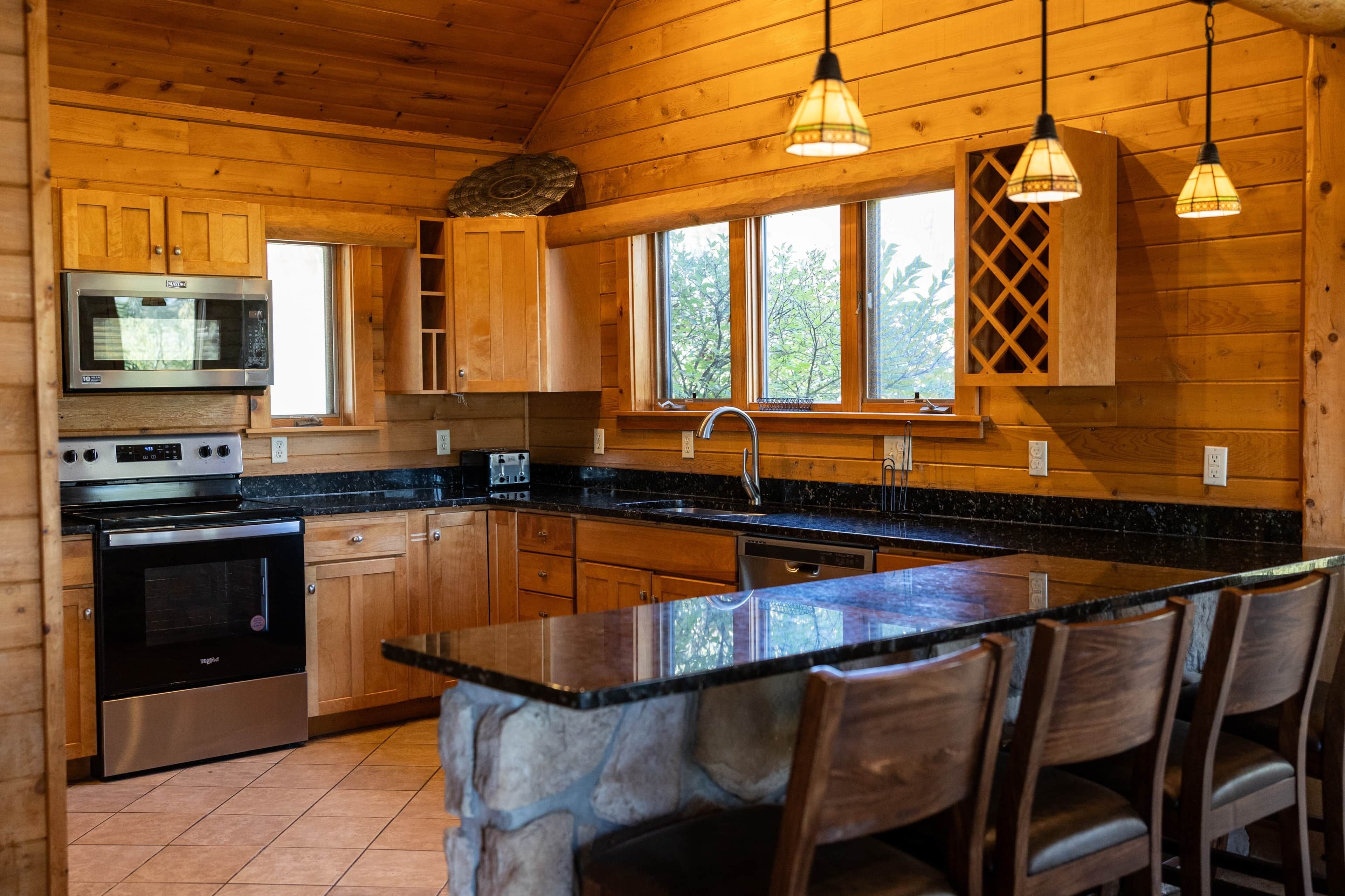 Cocina de cabaña de madera con isla central, microondas integrado, estufa y lavavajillas.