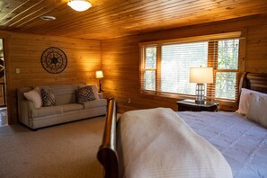 Een knus houten kamer met een houten plafond, een bed, een slaapbank en een raam met zonwering.