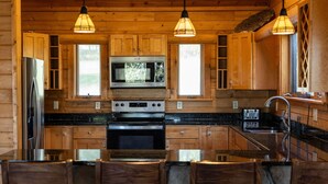 A wooden cabin interior with a kitchen featuring a refrigerator, microwave, stove, and dining area with chairs and a table. - Splash Mountain 6 bedrooms with indoor pool & mountain and filtered lake view (Garrett County)