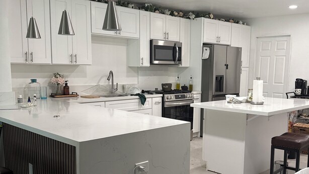 Una cocina moderna con armarios blancos, electrodomésticos de acero inoxidable e iluminación colgante.