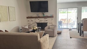Una sala de estar con un sofá color crema, una chimenea, un televisor de pantalla plana y vistas al exterior.