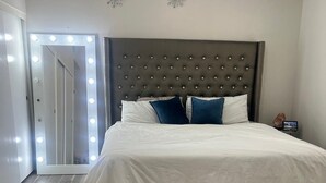 Un dormitorio con una cama grande, cabecera capitonada y tocador con luces.