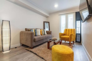 Ein Wohnzimmer mit einer Couch, einem Sessel, einem Hocker und einer Stehlampe.