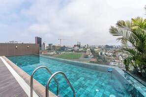 Piscina infinita en la azotea con vistas a la ciudad, una palmera y cielo despejado.