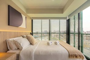 Una habitación de hotel moderna con una cama grande, cabecera, una obra de arte colgada en la pared y vistas a través de ventanales de piso a techo.