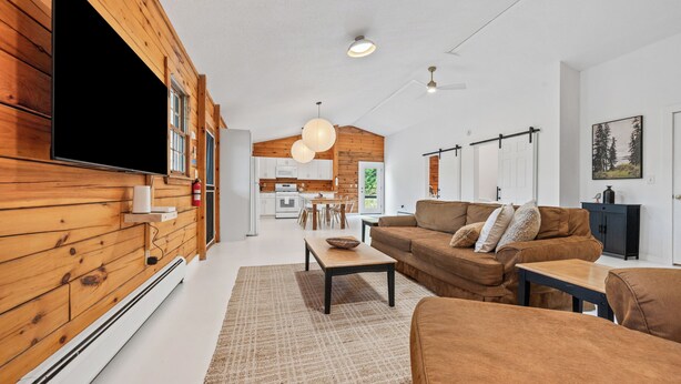 Un salon moderne avec un mur en bois, un téléviseur à écran plat, un canapé marron et un coin repas à l’arrière-plan.