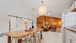 Une cuisine moderne avec un mur d’accent en bois, un coin repas avec des chaises transparentes et une grande table en bois.