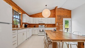 Une cuisine moderne avec des meubles blancs, un plafond en bois et une grande table à manger entourée de chaises.