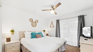 A bedroom with a bed, nightstands, a ceiling fan, a TV, and a window with curtains. - Resort stay~Pool Access~Peaceful Retreat~Balcony (Kissimmee)
