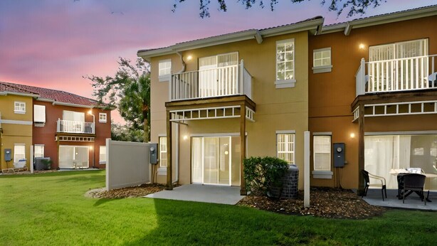 A two-story residential building with a well-maintained lawn, a covered patio, and a small outdoor seating area. - Resort stay~Pool Access~Peaceful Retreat~Balcony (Kissimmee)