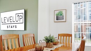 A dining area with a wooden table, four chairs, a sign that reads "LEVEL UP STAYS", and a framed plant on the wall. - Resort stay~Pool Access~Peaceful Retreat~Balcony (Kissimmee)