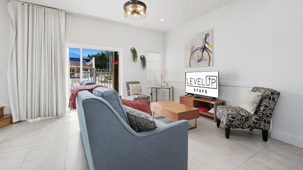 A modern living room with a sofa, armchair, and coffee table. A television is mounted on the wall, and there is a sign that reads "LEVEL UP STAYS". - Direct resort access~Balcony~Pool~Upgraded Inside (Kissimmee)