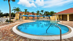A swimming pool with lounge chairs and umbrellas, surrounded by palm trees and buildings with red-tiled roofs. - Direct resort access~Balcony~Pool~Upgraded Inside (Kissimmee)