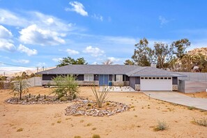 A single-story house with a garage, a front yard with a rock garden, and a clear blue sky.