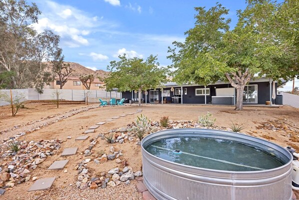 A residential area with a swimming pool, outdoor seating, and a hilly landscape in the background.