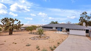 A residential property with a single-story house, a paved driveway, and a landscaped garden with desert plants. - Casa Cosmic: Hot Tub, Fire Pit & Stargazing (Joshua Tree)