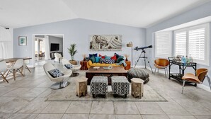 A spacious living room with a sofa, ottomans, and a coffee table. There is a dining area with chairs and a table. - Casa Cosmic: Hot Tub, Fire Pit & Stargazing (Joshua Tree)