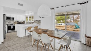 A modern kitchen with white cabinets, a wooden dining table, and a large window. - Casa Cosmic: Hot Tub, Fire Pit & Stargazing (Joshua Tree)