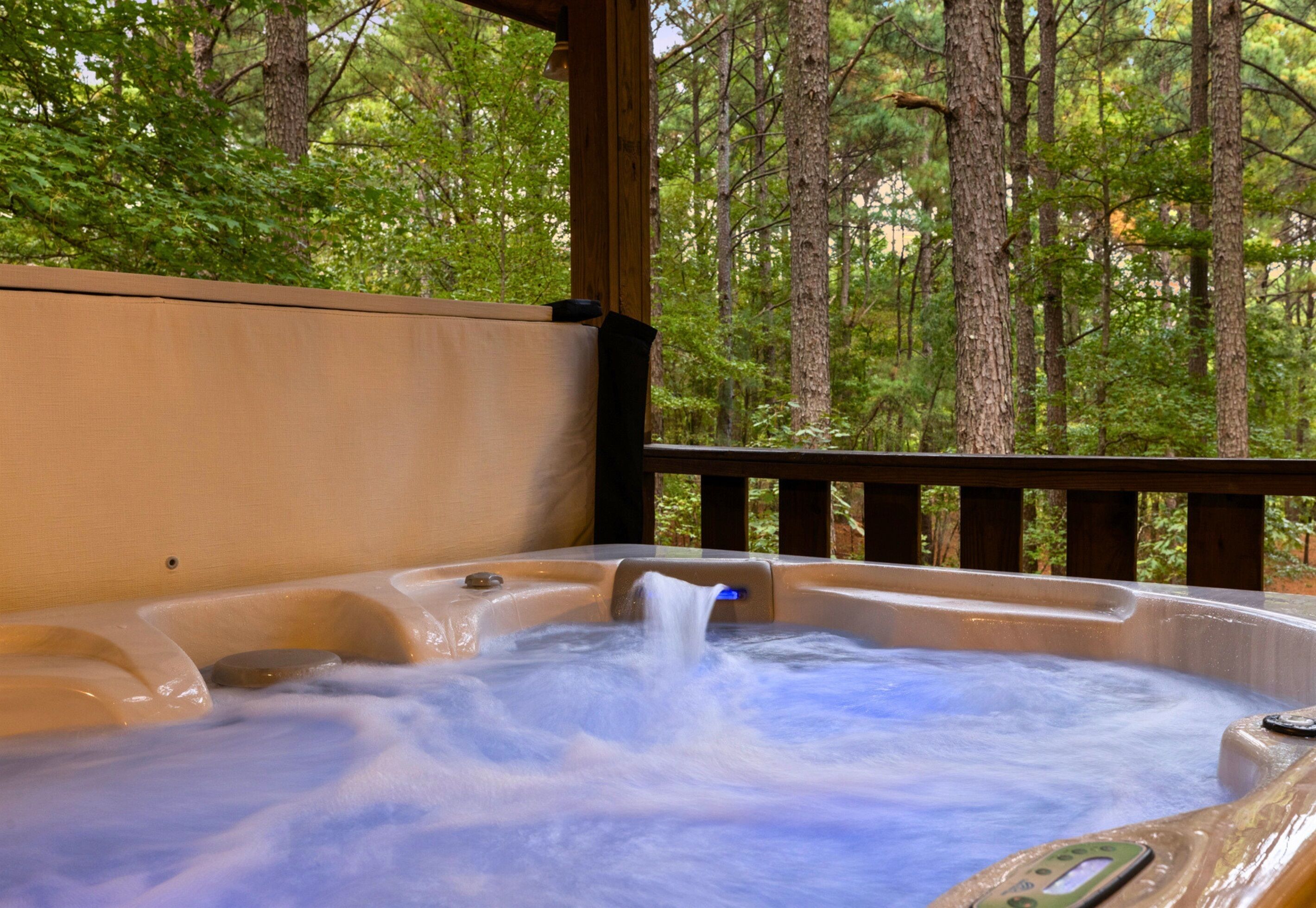 A hot tub with a wooden deck and a view of a forest.