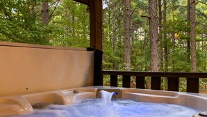 Un bain à remous avec une terrasse en bois et vue sur une forêt.