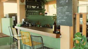 A bar area with a chalkboard menu, bar stools, and a kitchen in the background. - Hotel Posada Girasol (Puerto Escondido)