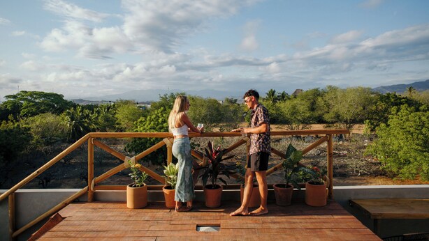 A wooden deck with potted plants and a railing overlooking a landscape with trees and mountains. - Hotel Posada Girasol (Puerto Escondido)