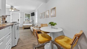 A modern kitchen with white cabinets, a wooden countertop, and a ceiling fan. There is a dining area with a round table and yellow chairs.