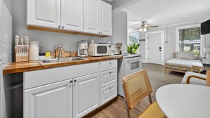 A modern kitchen with white cabinets, a wooden countertop, and a dining area with a white table and wicker chairs.