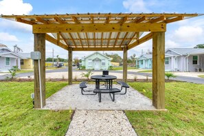 Un área de estar al aire libre cubierta con una mesa y bancos, rodeada por una pérgola de madera y grava.