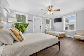 Un dormitorio con una cama grande, dos camas más pequeñas, un ventilador de techo y un televisor en la pared.