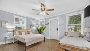 A bedroom with a bed, bedside tables, a ceiling fan, and large windows.