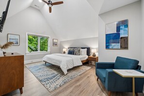 Un dormitorio con cama, escritorio, sofá azul, ventilador de techo y obras de arte en las paredes.