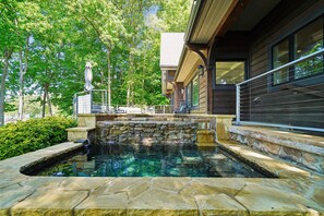 Una piscina de piedra con un muro de piedra, rodeada de árboles y un edificio con balcón.