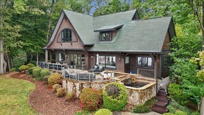 A large, two-story log cabin with a stone foundation, a deck, and a hot tub.