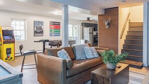 A modern living room with a brown leather sofa, a coffee table with a plant, and a staircase with a mounted deer head. - NEW LISTING! Heated Pool + Sauna + Hot Tub + Game Room + Jungle Gym + Fire Pit (Windham)