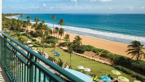Ein Balkon mit Blick auf einen Strand, Palmen und einen Poolbereich.