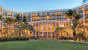Ein mehrstöckiges Hotel mit Innenhof, Palmen und gepflegtem Rasen.