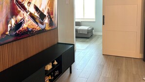 A modern living room with a large flat-screen TV mounted on a wooden wall, a sliding glass door leading to another room, and a wooden floor. - Bright Modern Condo Near SkyTrain & Hospital (New Westminster)