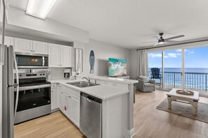 A modern kitchen with stainless steel appliances, a dining area with a view of the ocean, and a balcony with a chair.