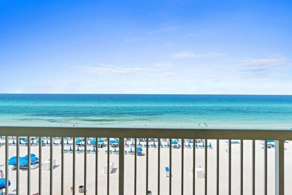 A beach view with a railing, beach umbrellas, and lounge chairs.